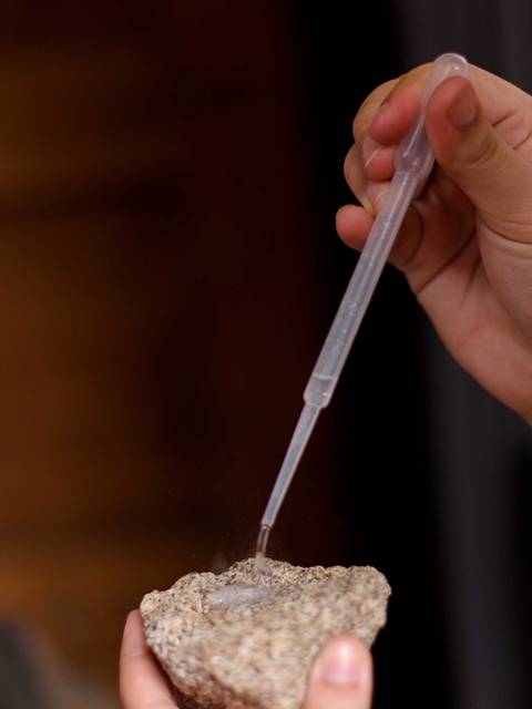 Una mano sostiene una piedra mientras utiliza un gotero para aplicar un líquido.