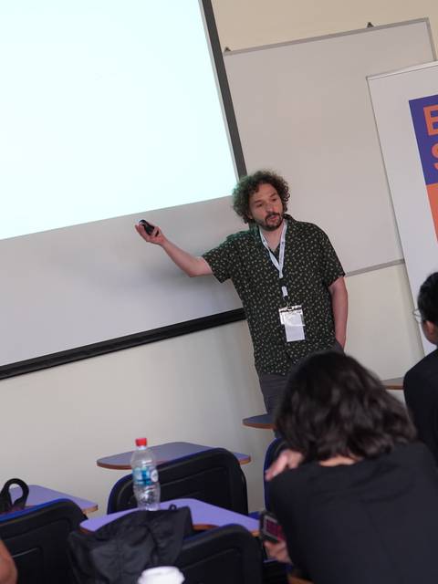 Un presentador expone un tema en una sala mientras el público lo escucha atentamente.