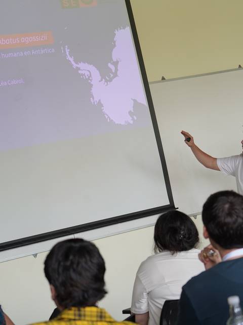 Un hombre presenta un tema en una conferencia mientras el público lo observa atentamente.