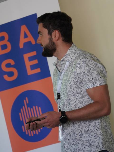 Un hombre está de pie frente a un banner que dice 'BASE'.