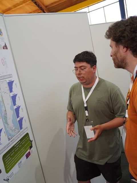 Dos personas discutiendo frente a un póster informativo en un evento académico.