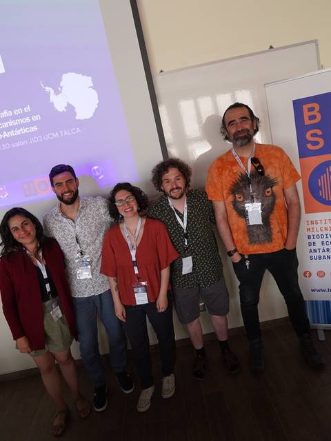 Un grupo de cinco personas posando en un evento académico con una presentación de fondo.