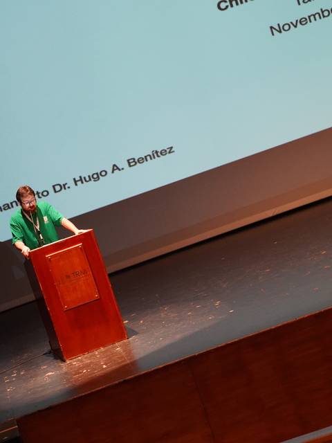 Una persona da una charla desde un podio en un escenario iluminado.