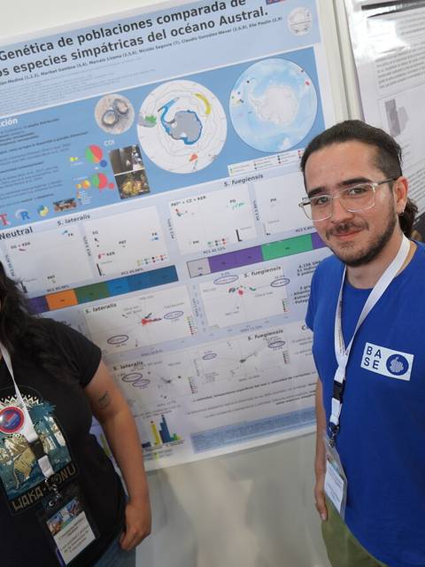 Dos personas posan frente a un cartel de investigación científica en un evento académico.