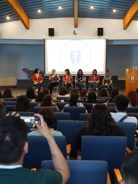 Una conferencia en un auditorio con varias personas presentes y panelistas en el escenario.