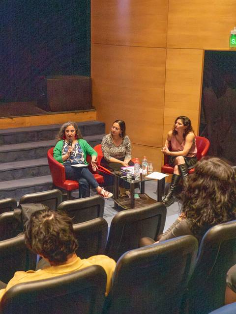 Tres mujeres participan en una conversación en un evento mientras el público las escucha.