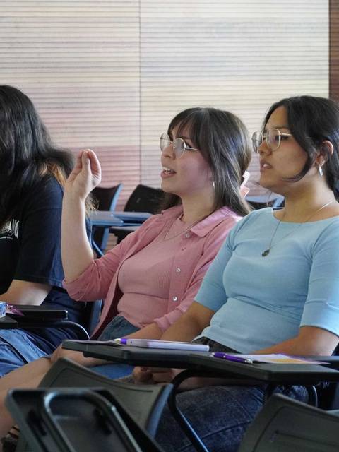 Un grupo de jóvenes mujeres están sentadas en un salón de clases prestando atención a una presentación.
