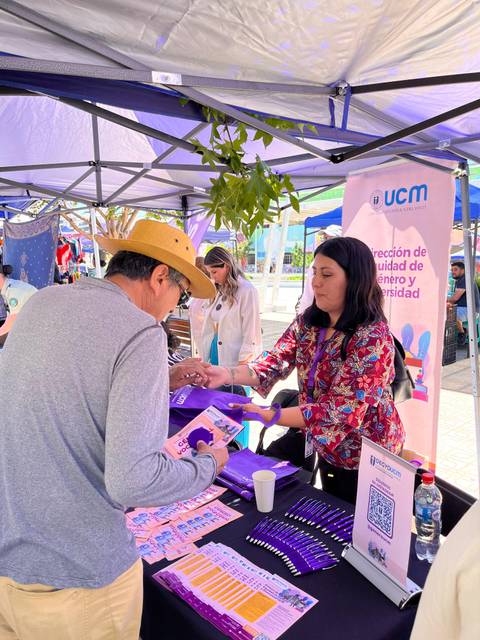Un hombre interactúa con una mujer en un stand, donde se distribuyen materiales informativos sobre género y diversidad.