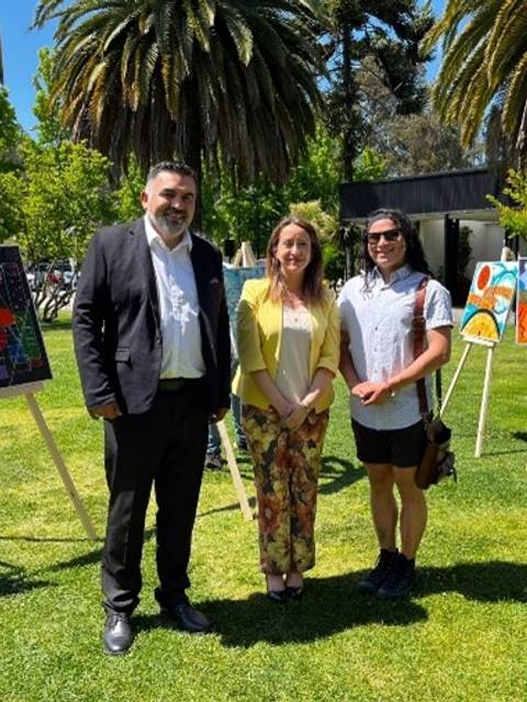 Tres personas posan en un evento al aire libre rodeados de obras de arte en un jardín.