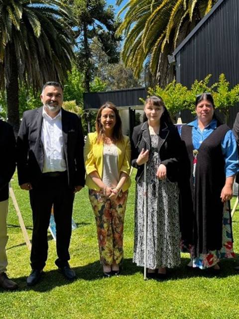 Un grupo de seis personas posando en un entorno al aire libre, rodeados de palmeras y cuadros en exhibición.