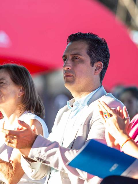 Un grupo de personas aplaudiendo en un evento al aire libre bajo una sombrilla roja.