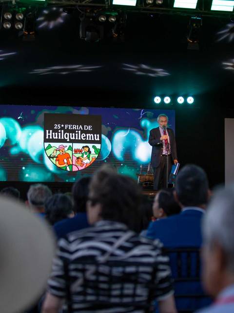 Un orador en el escenario durante la 25ª Feria de Huilquilemu frente a un público atento.