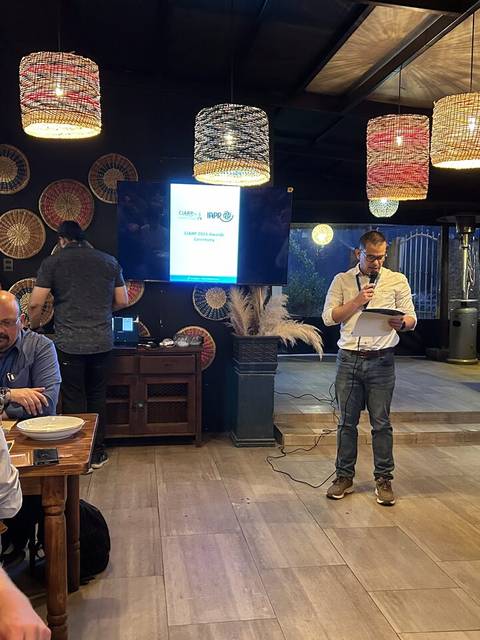 Un grupo de personas en un restaurante mientras alguien da un discurso en el centro.