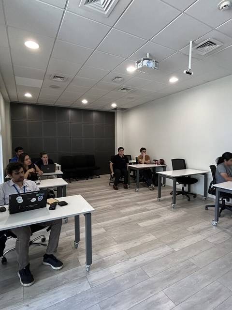 Un aula moderna con estudiantes sentados en escritorios y una instructora presentando frente a ellos.