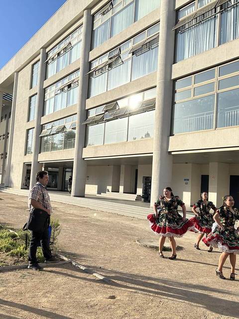 Un grupo de personas vestidas con trajes típicos baila enfrente de un edificio moderno.