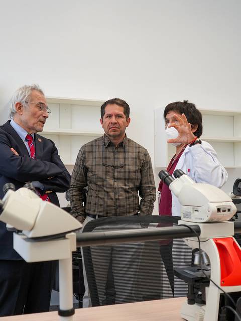 Tres personas conversan en un laboratorio con microscopios.