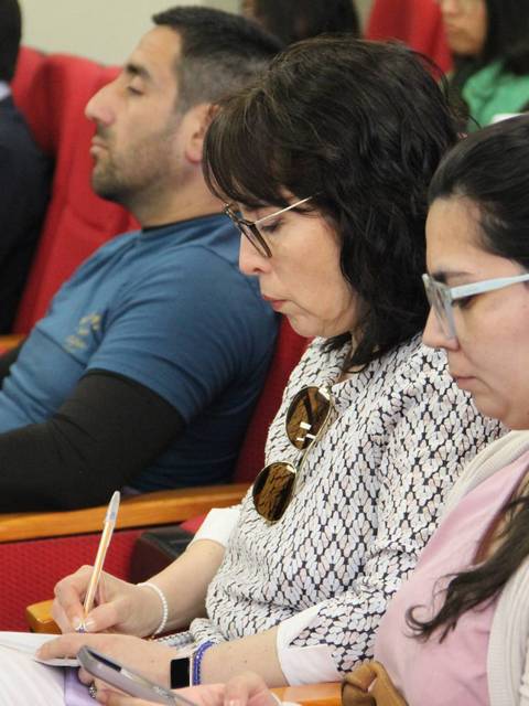 Un grupo de personas atendiendo una conferencia en un salón con sillas rojas.