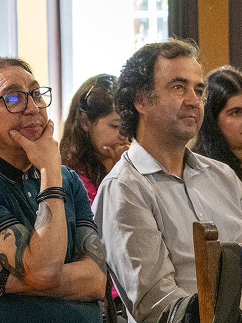 Un grupo de personas sentadas en una sala, prestando atención a un evento.