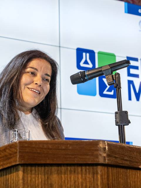 Una mujer sonriente habla en un evento frente a un micrófono.