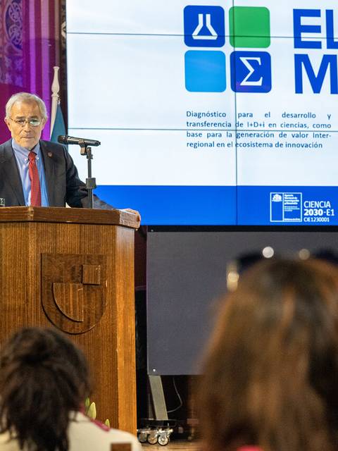 Un ponente hablando en un evento con un fondo que exhibe el logo de un programa relacionado con la ciencia y la innovación.