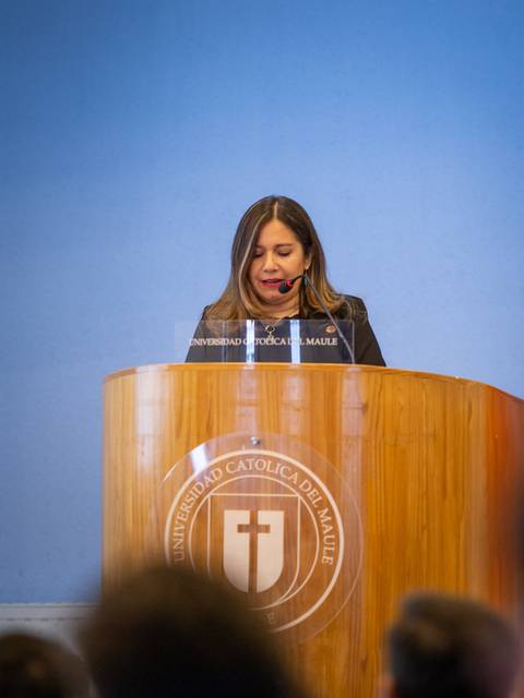 Una mujer habla desde un estrado en un evento formal frente a una audiencia.