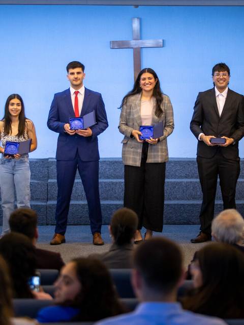 Un grupo de graduados posan en un evento ceremonial frente a una cruz.