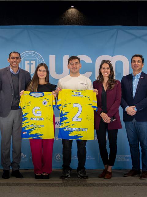 Un grupo de personas sostiene camisetas de un equipo en un evento junto a un fondo con el logo de UCM.