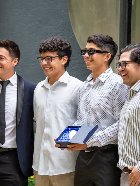 Un grupo de cuatro jóvenes posando juntos con una medalla en el exterior.