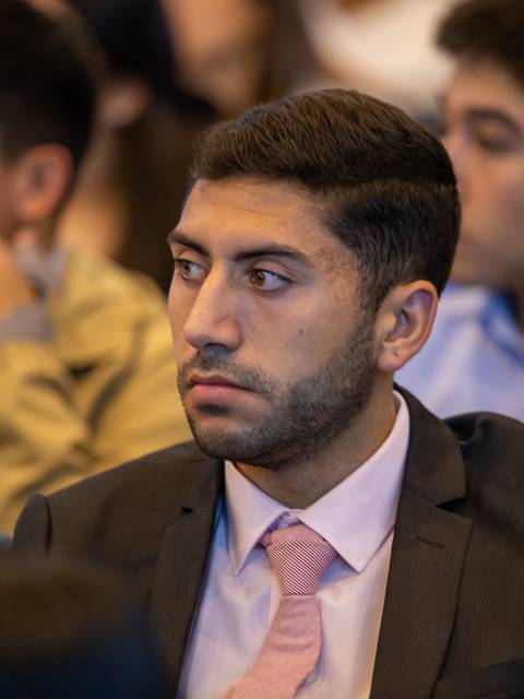 Un hombre con traje oscuro y corbata rosada escucha atentamente en un evento.