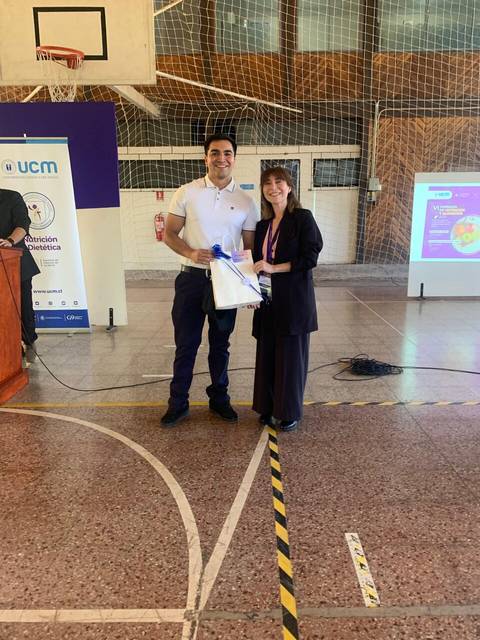 Un hombre y una mujer están en un evento, donde él está recibiendo un regalo de ella.