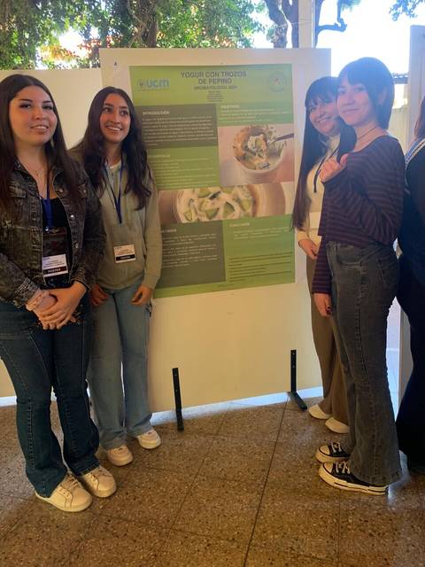 Un grupo de jóvenes posan junto a un cartel informativo sobre un proyecto relacionado con el aprovechamiento del pepino.