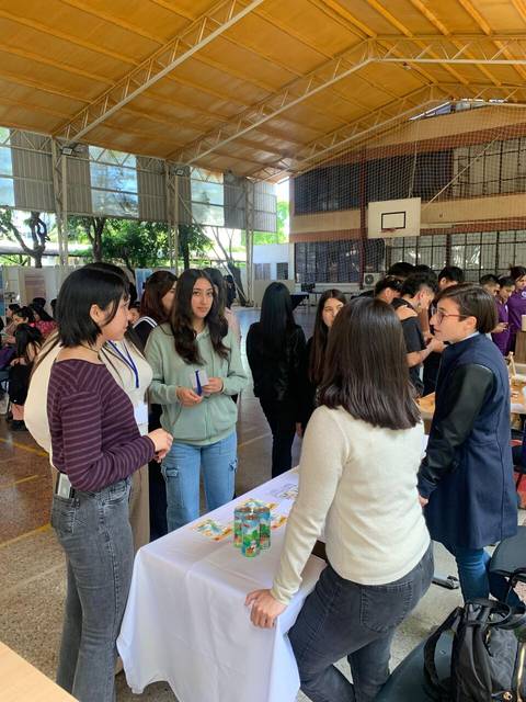 Un grupo de estudiantes interactuando en un evento dentro de un gimnasio escolar.