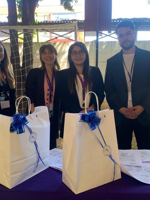 Un grupo de cuatro personas sonrientes se encuentra frente a una mesa con bolsas decoradas.