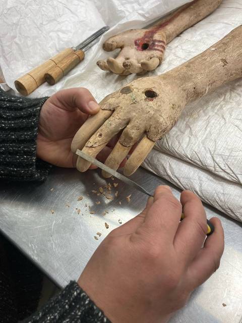 Una persona está trabajando en la restauración de una mano de una figura, utilizando herramientas específicas.