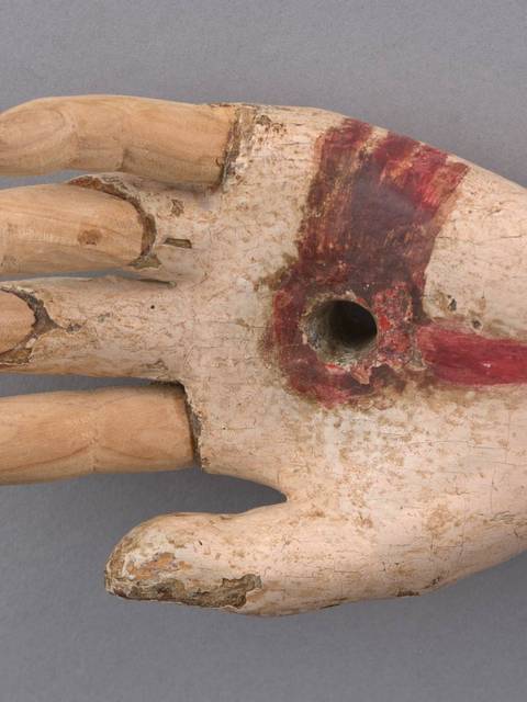 Se muestra una mano de madera decorada con pintura roja y un agujero en la palma.