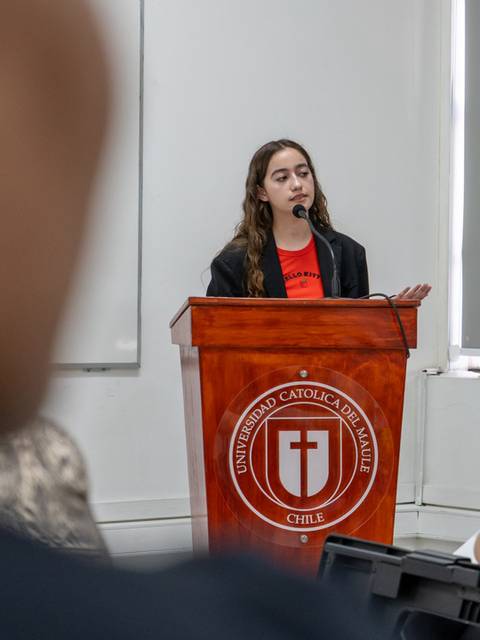 Una joven está hablando frente a un público en un evento académico.