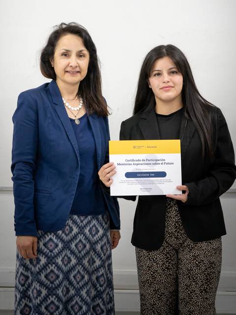 Dos mujeres posan sonrientes sosteniendo un certificado en un entorno formal.