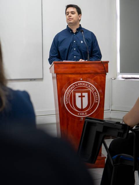 Un hombre está dando una charla frente a un podio en una sala de clases.