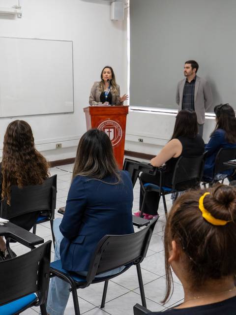 Una presentación en un salón de clases con un grupo de personas escuchando a dos expositores.