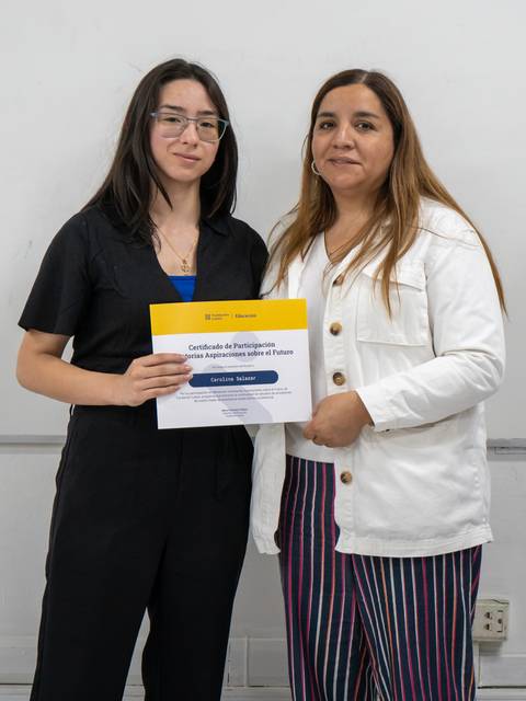 Dos mujeres posan juntas sosteniendo un certificado en un entorno académico.