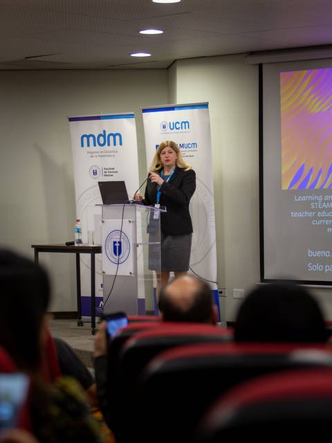 Una mujer está dando una conferencia en un auditorio mientras la audiencia la escucha atentamente.
