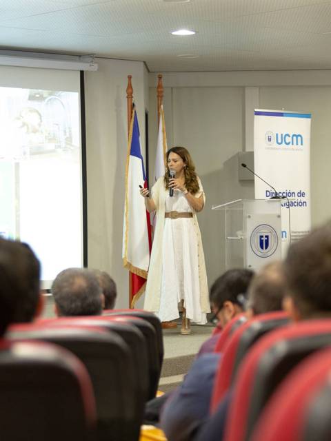 Una mujer presenta un proyecto frente a un auditorio en un evento académico.
