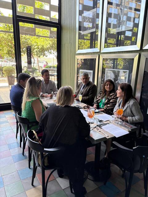 Un grupo de personas se reúne en una mesa en un restaurante, disfrutando de bebidas y comida mientras conversan.