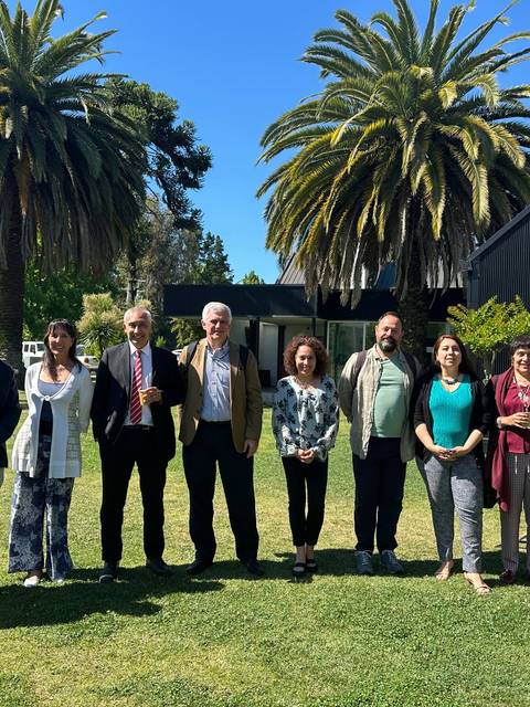 Un grupo de personas posando en un jardín con palmeras y un edificio al fondo.