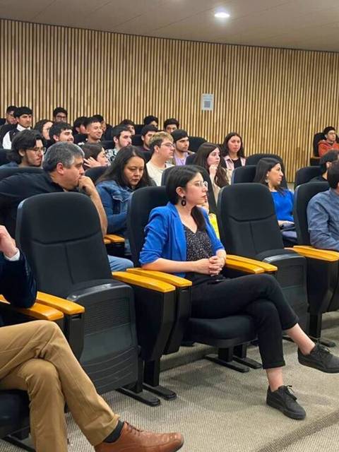 Un grupo de personas sentadas en un auditorio prestando atención a una presentación.