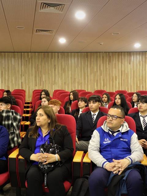 Un grupo de estudiantes y profesores sentados en un auditorio durante una presentación.