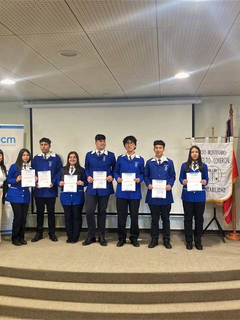 Un grupo de estudiantes en una ceremonia de entrega de certificados, con personal del evento a su lado.
