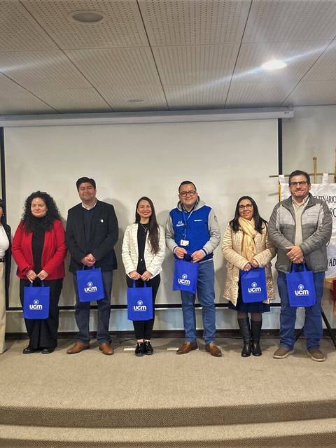 Un grupo de personas posando en un evento académico en la UCM, con bolsas de la institución.