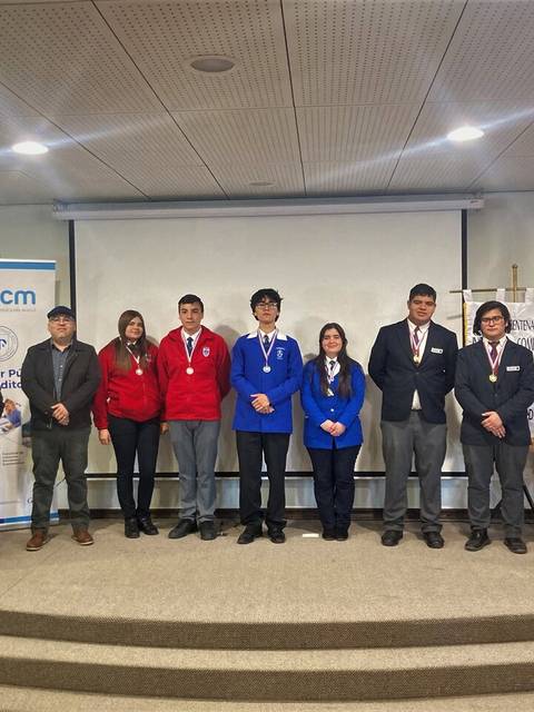 Grupo de personas posando en un escenario, todos con medallas y vestidos formalmente.