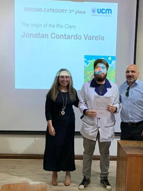 Un grupo de tres personas sonríe frente a una presentación en la que se destaca un premio de tercer lugar.